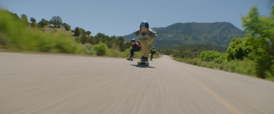 Three people skateboard down a rural road