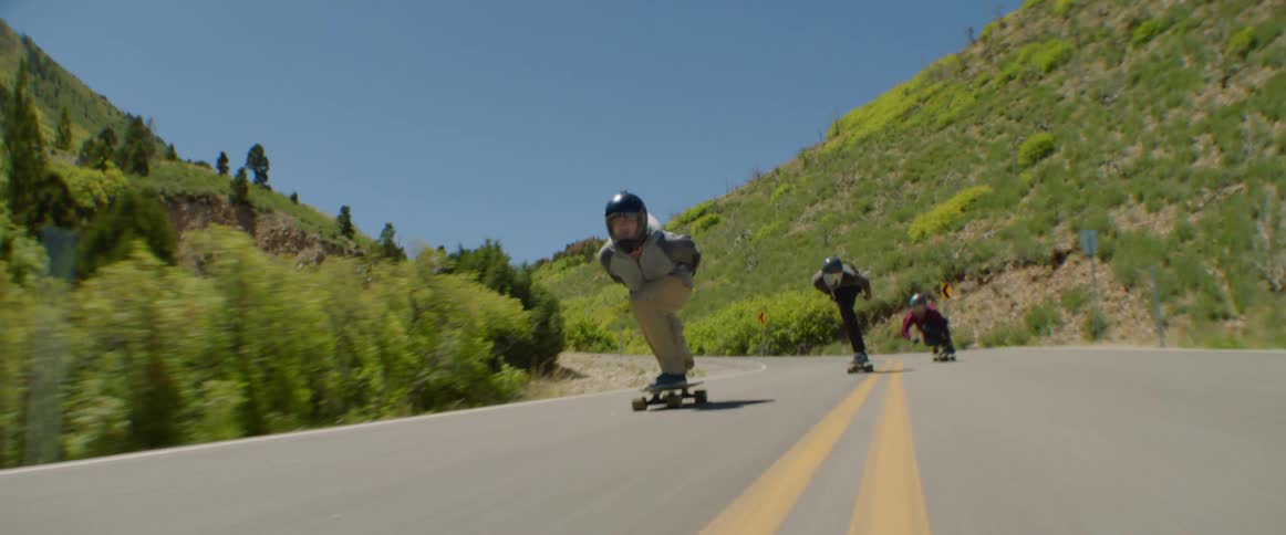 Group of friends wearing crash helmets and protective gloves riding skateboards downhill at full speed