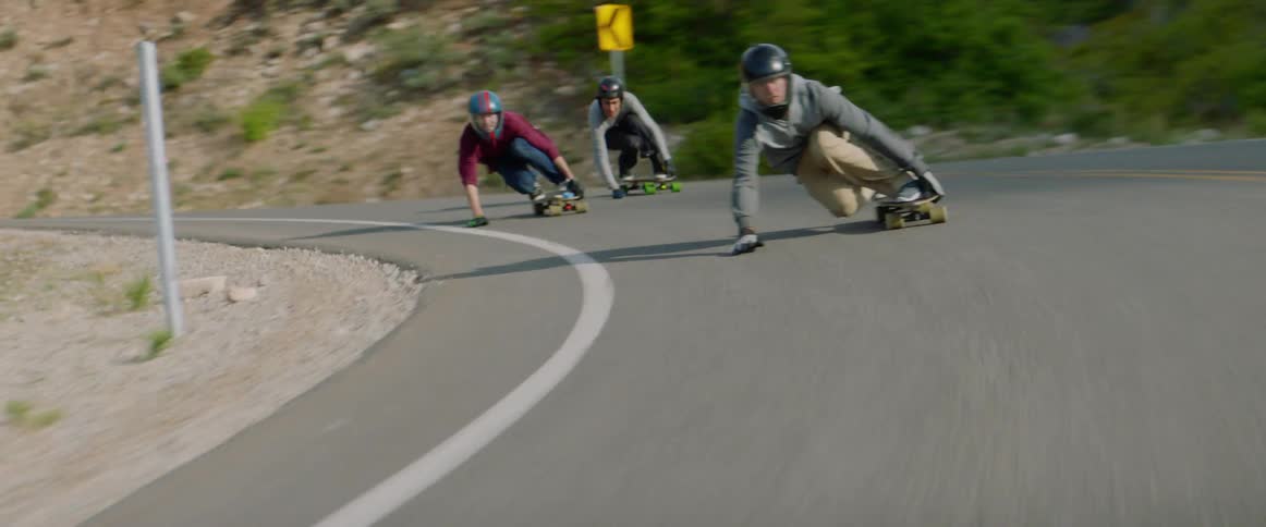 People with helmet and gloves skating down a road on skateboards