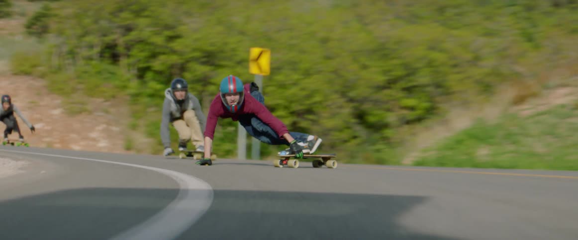 Skateboarders ride downhill on a winding road at high speed