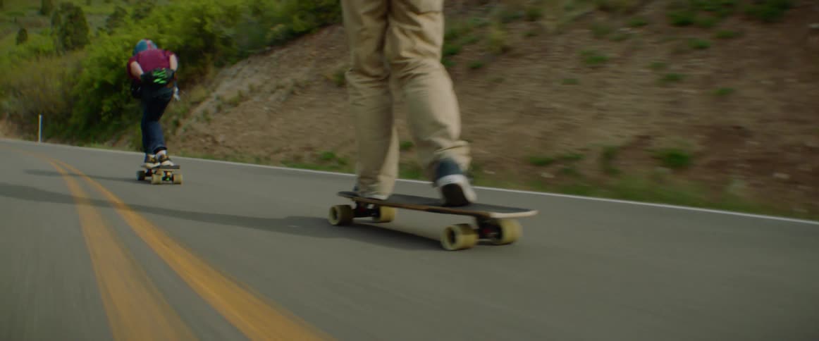 Three people are long boarding down the road
