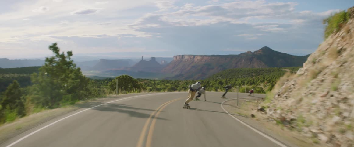 Skateboarders speeding down a paved road on a mountainside