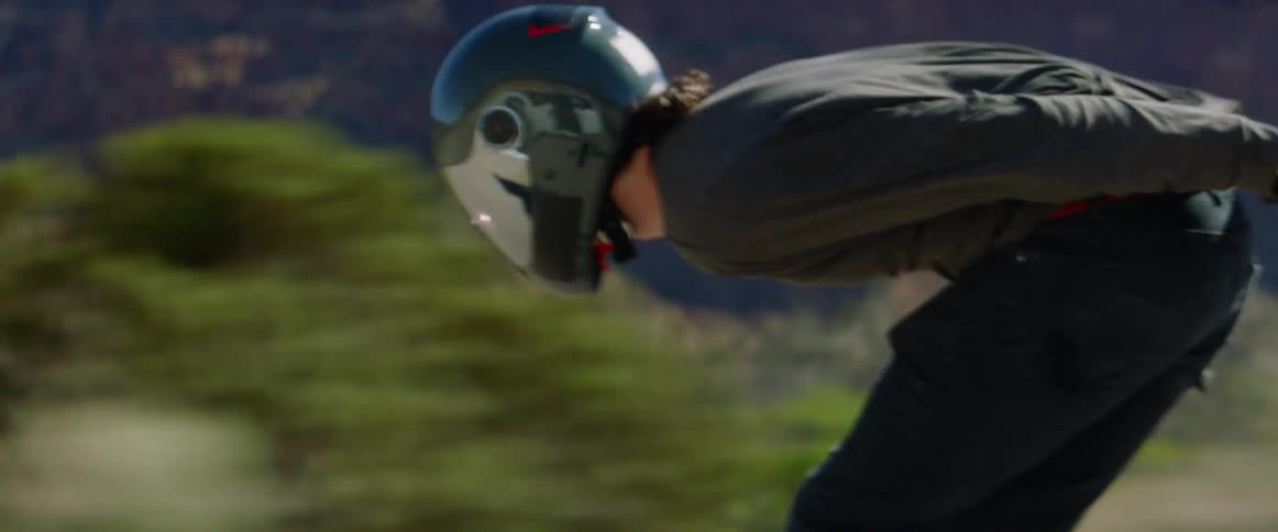 Man with a helmet rides a skateboard at high speed on a country road with mountains in the background