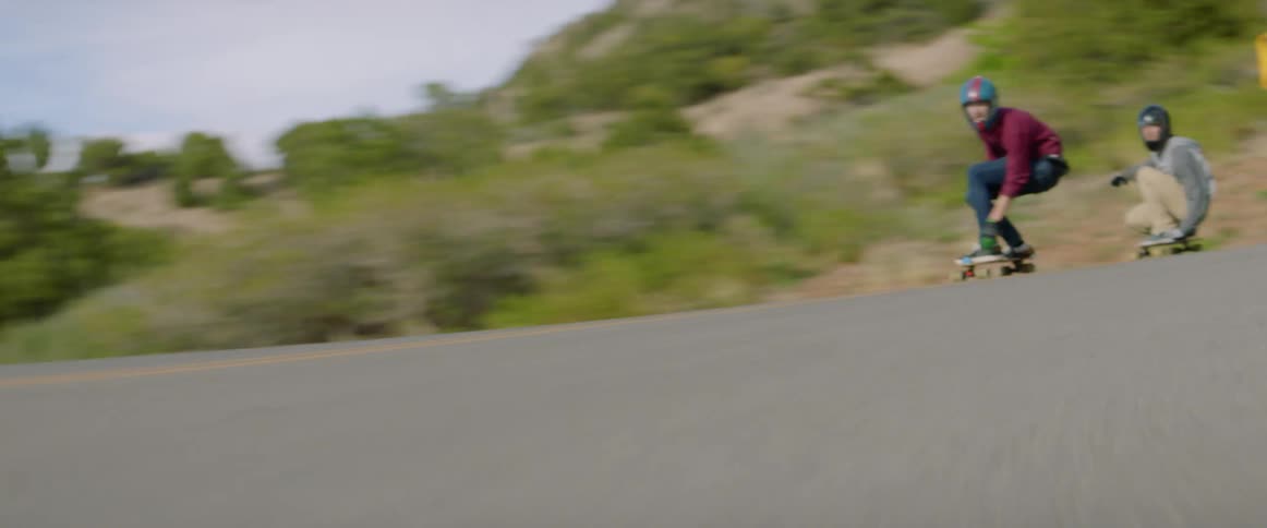 Skateboarders speeding down a hillside road on a summer day