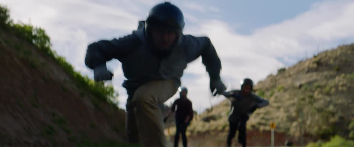 Three man with helmets ride skateboards by pushing their foot on the ground