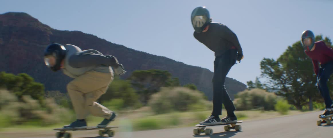 Three people speed skateboard down a rural road
