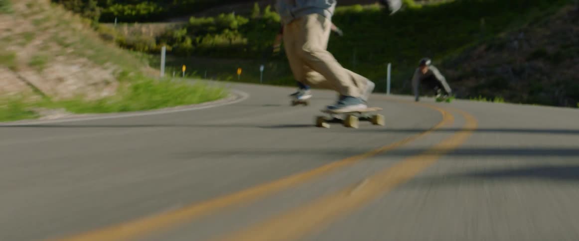 Three people skateboard on a rural hillside road