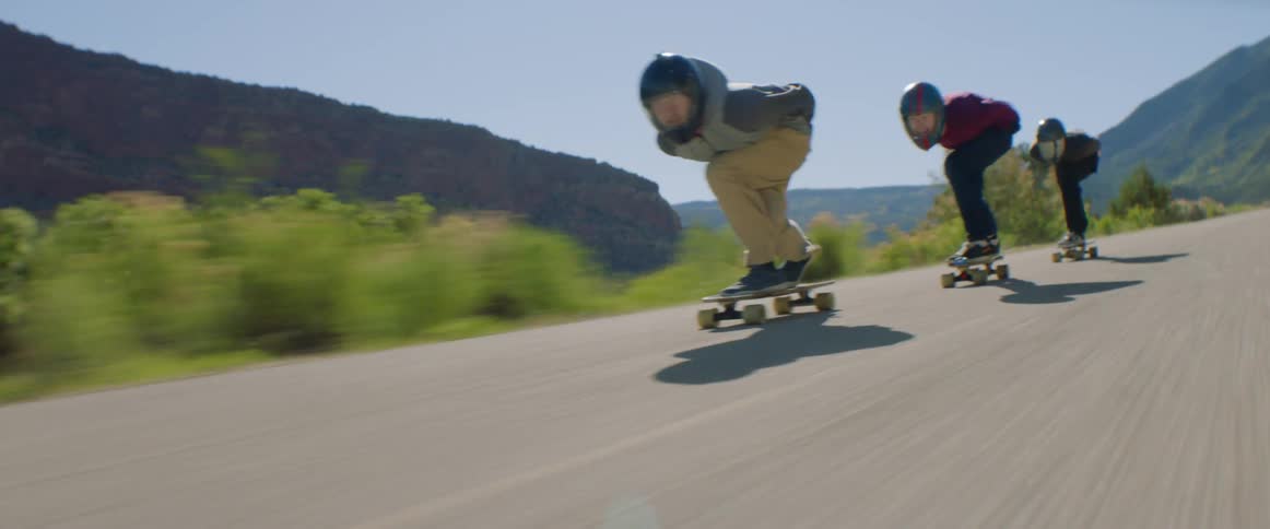 People with helmet and gloves skateboarding down a road