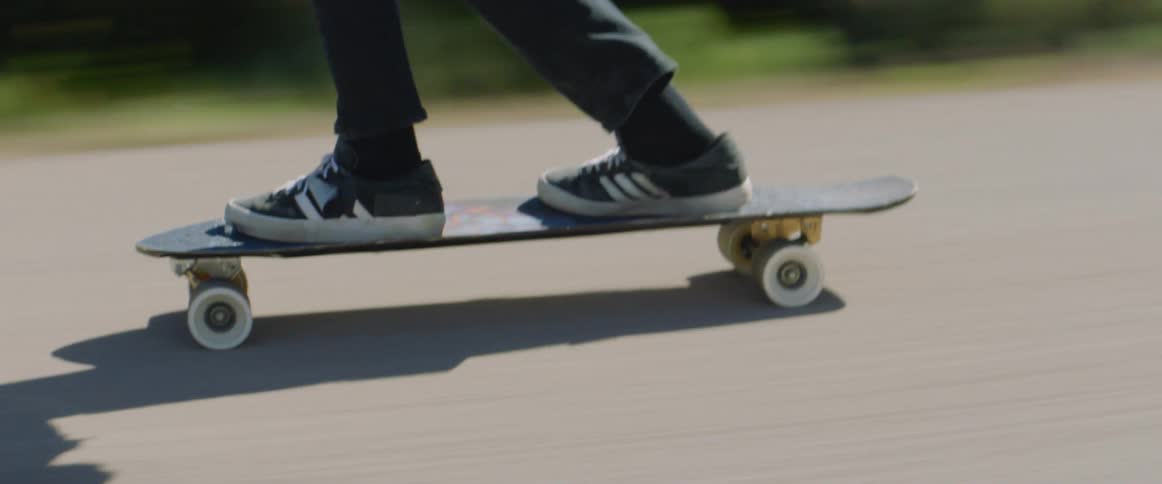 A skateboarder speeding on a paved road in summer