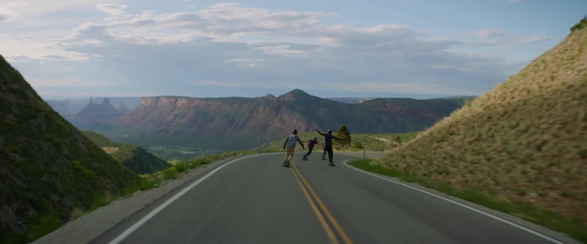 Skateboarders ride skateboards down on a winding mountain road