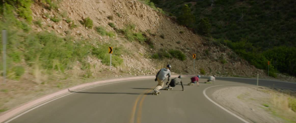Skateboarders ride downhill on a winding road at high speed in the mountains