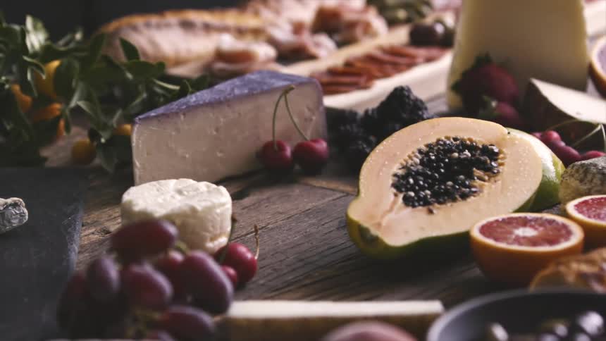 A person takes a bottle of wine off a table covered in fruit and cheese