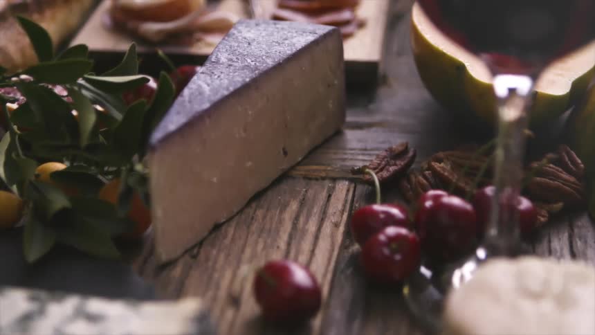 A wooden table is covered in an impressive spread of cheeses meat and fruits