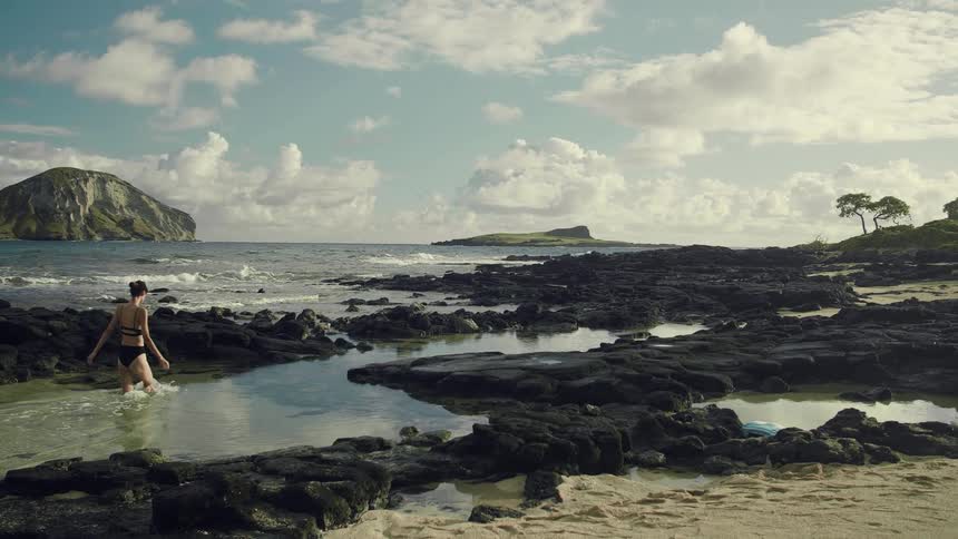 A woman with a bathing suit walking on a beach with the ocean sky and clouds in the background
