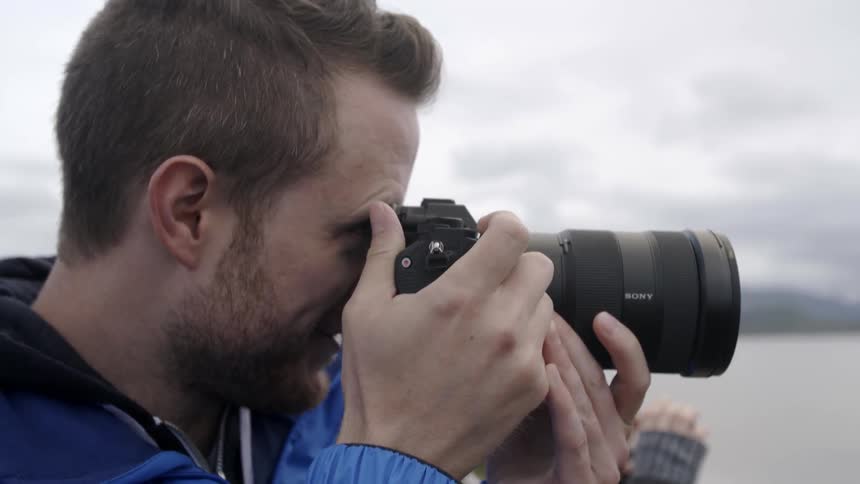 A man holding a camera to his eyes is talking and aiming the camera