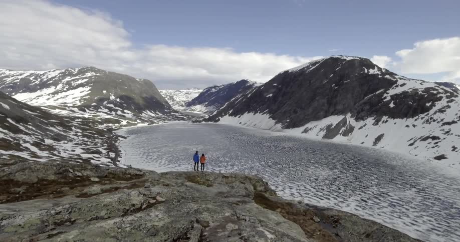 Two people stand on a cliff overlooking a mountain pass