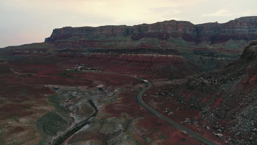 Vehicle travels through badlands past town toward bridge along winding road near ravine