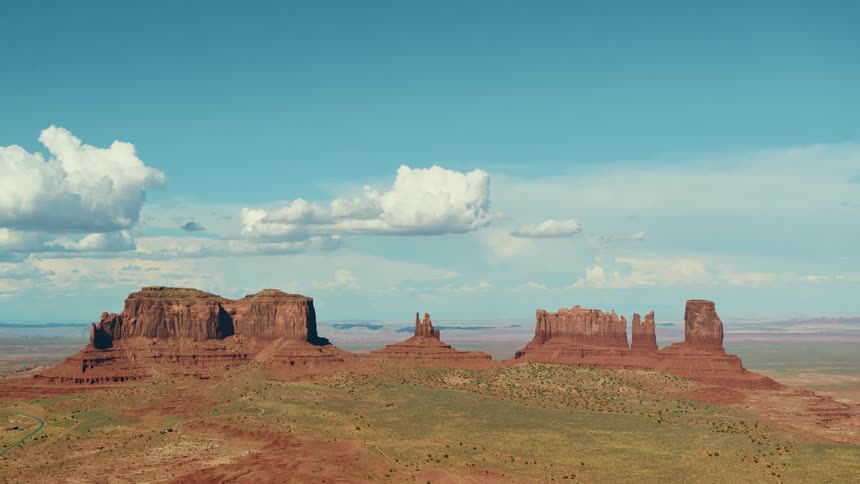 Fluffy clouds loom over a mesa surrounded by fields