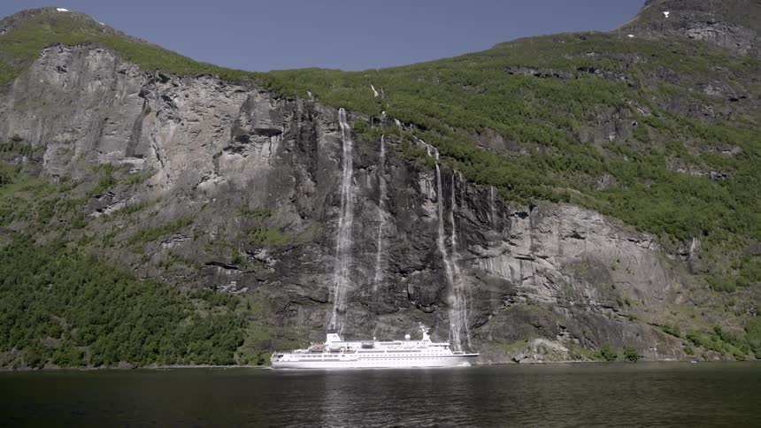 A large yacht moves along a steep cliff