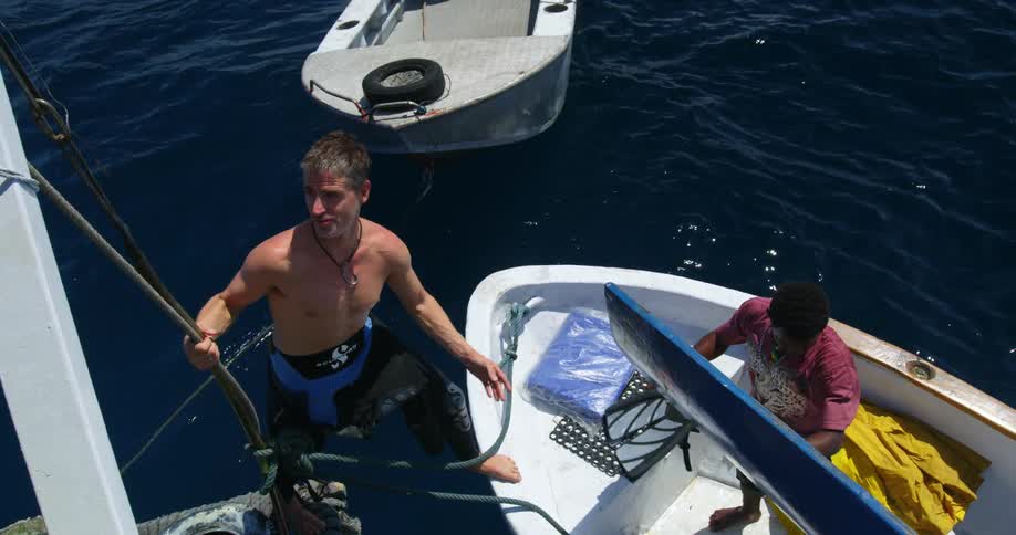 A man handing his flippers to another man on a boat
