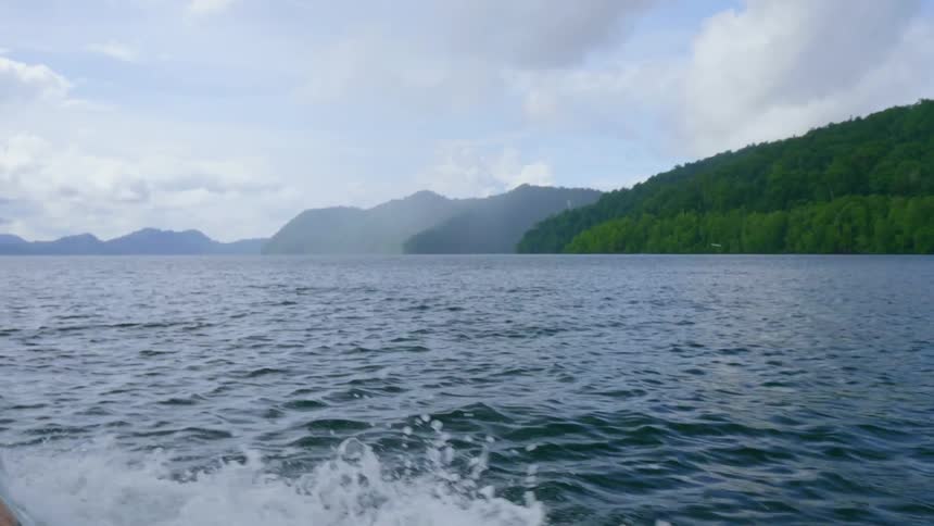The boat is traveling fast in the water near the hills