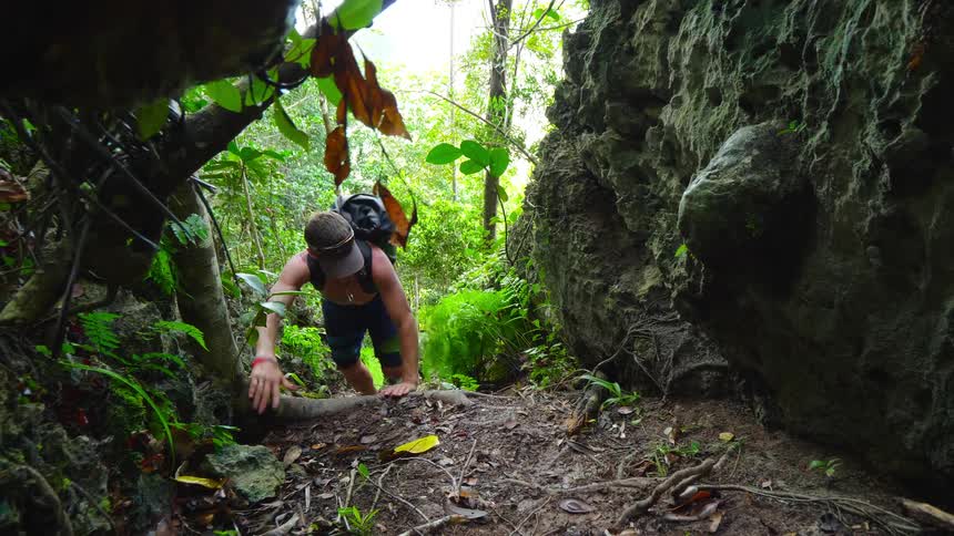 A man climbs up a small hill into a narrow gap in a woodland during the day