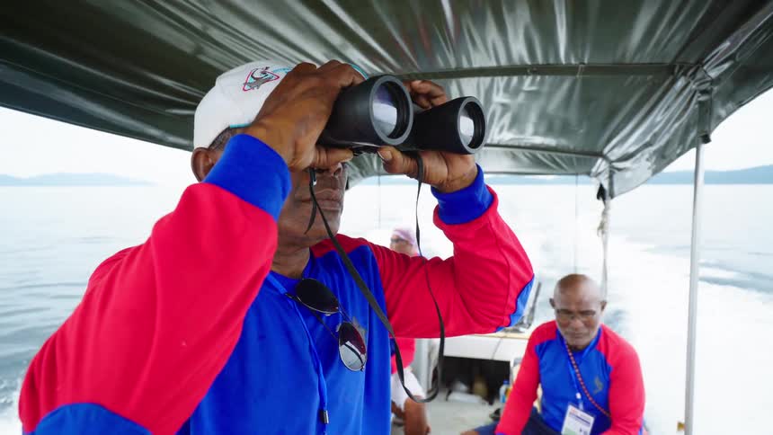 A ranger with a hat and binoculars standing on a boat with other men