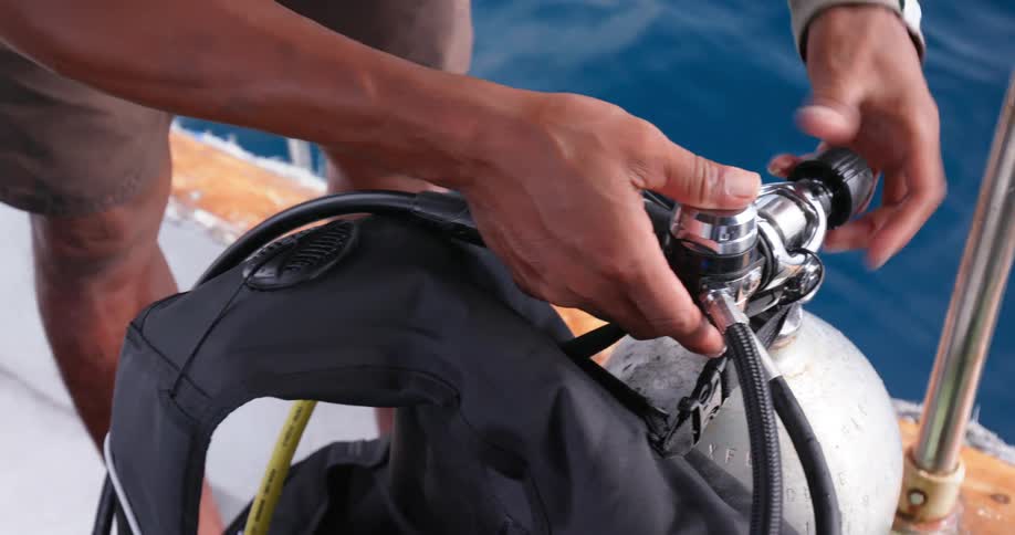 A man on a boat unscrews a knob on an oxygen tank