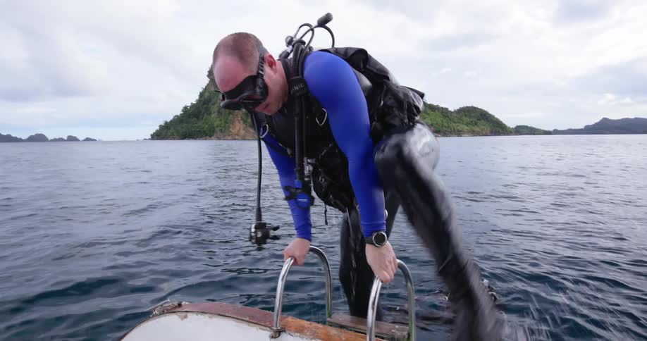 Two scuba divers climb a ladder and get back into their boat with tanks strapped to their backs