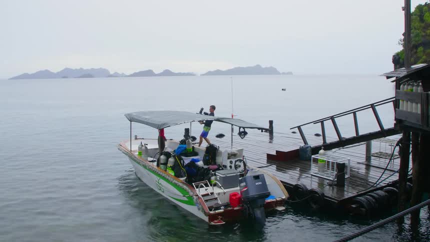 Men load motor boat floating at dock near misty forest covered shore