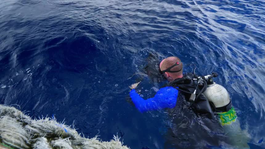 A man on a boat hands an underwater video camera to a diver in the ocean