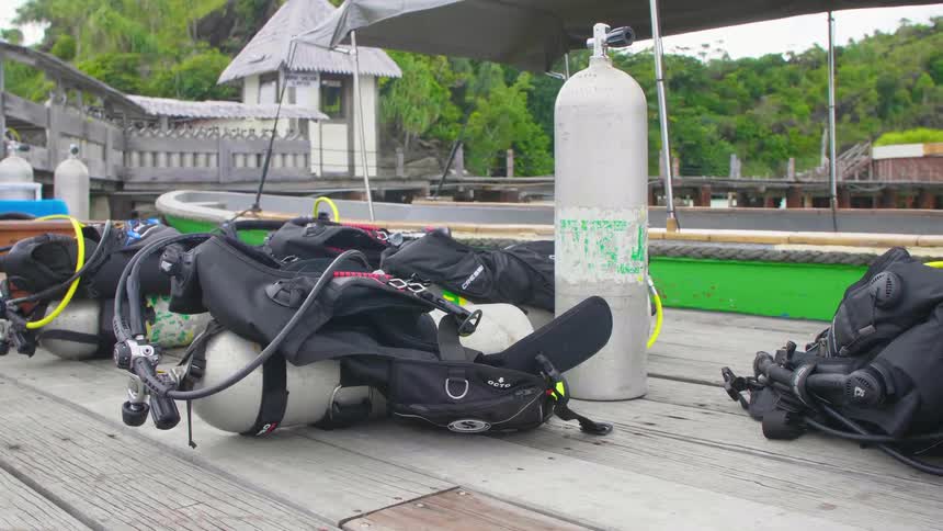 A dock with scuba equipment and air tanks next to a boat with trees the sky and clouds in the background