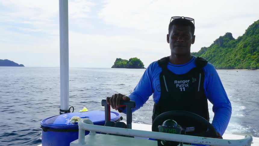 A water patrol officer steers a boat in the ocean while wearing a safety vest