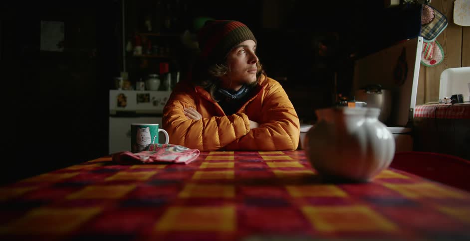 A man with a hat and coat sitting at a table with a mug