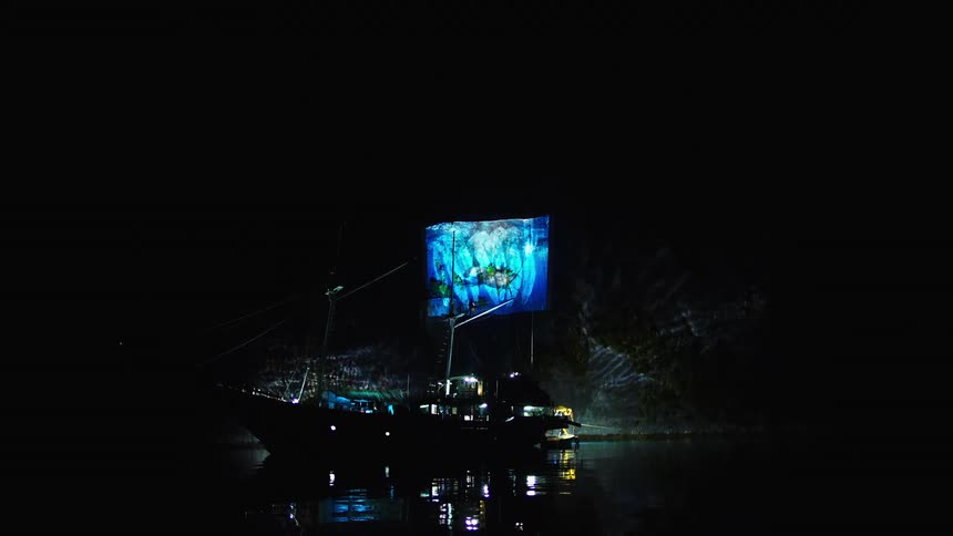 Projector plays on cliff behind sailing boat in the water