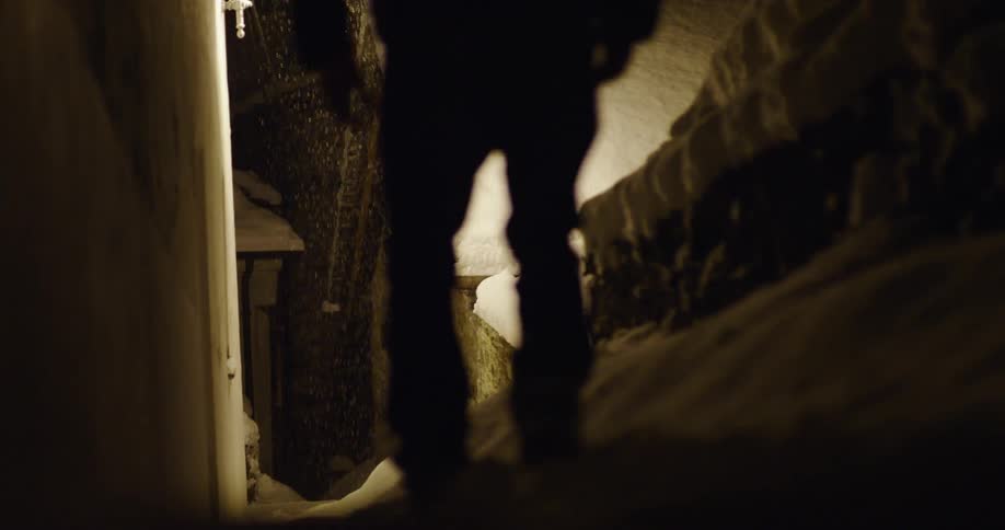 A man walks throw a narrow alleyway on a snowy night
