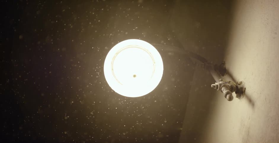 Snowflakes fall under bright light hanging on wall at night