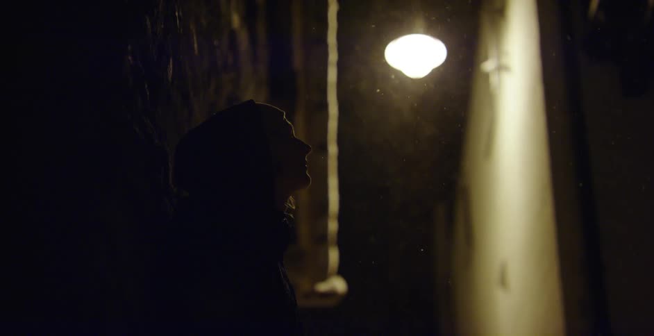 A person leans against a wall as snow falls outside