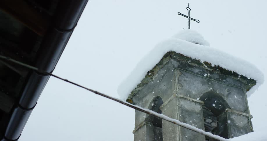Snow falling around a church tower with a cross on a winter day