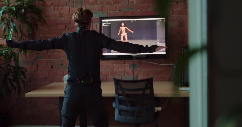 Man wearing vr goggles balances on board playing computer game facing screen showing his player character