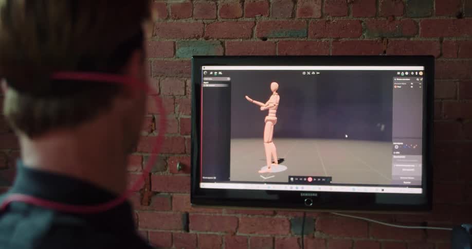 Man manipulates silver ball as motion capture displays same motions on screen against brick wall