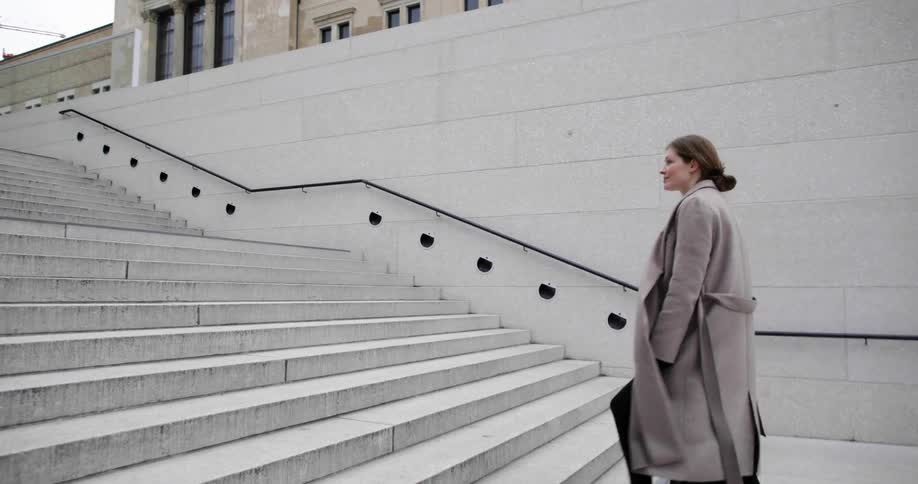 Woman walks up wide marble steps toward building with product display in front