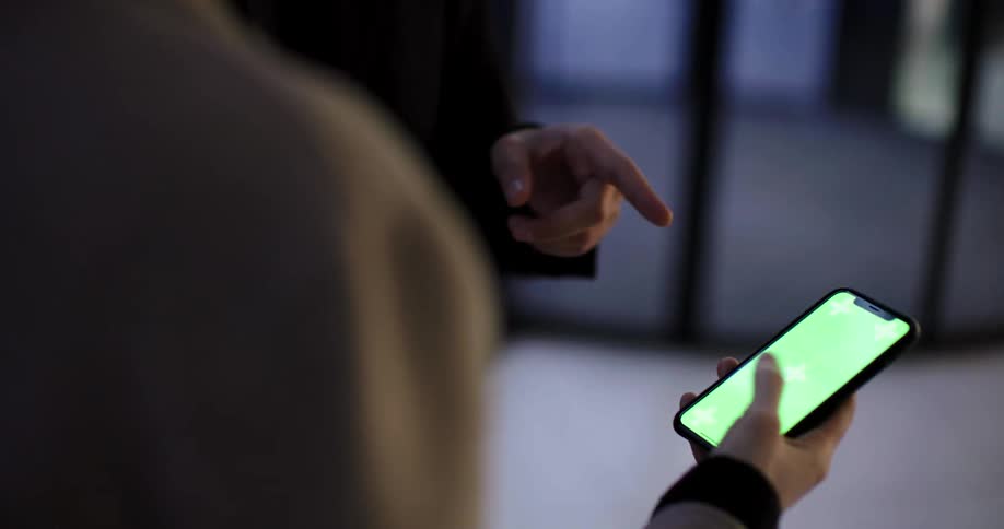 Two women talk in an office as one of them scrolls through an app