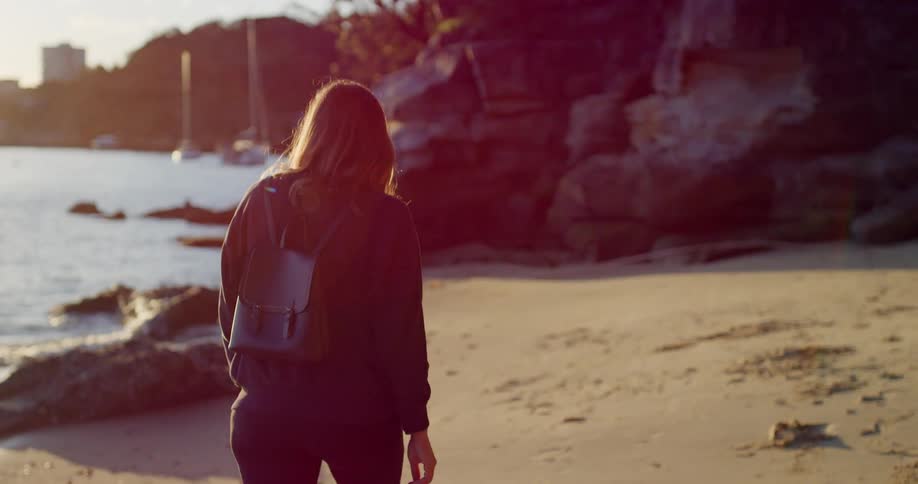 A woman walks along a rocky beach on a sunny day