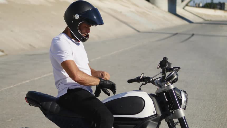 A man is sitting on his parked motorcycle outdoors