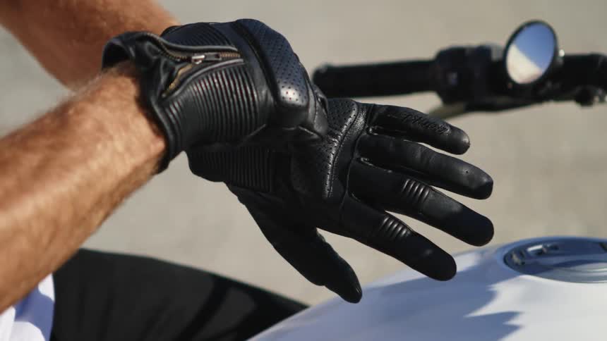 A man is putting on his gloves while sitting on a motorcycle