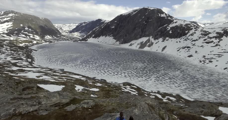 Two people looking towards a frozen lake in between snowy mountains
