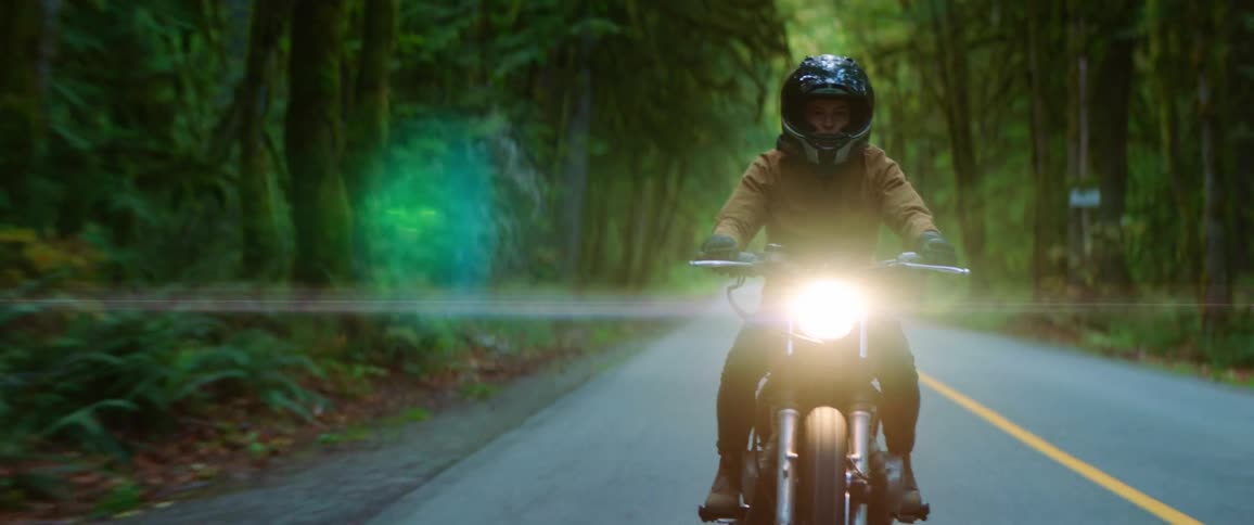 A motorcyclist in a helmet riding on a paved forest road