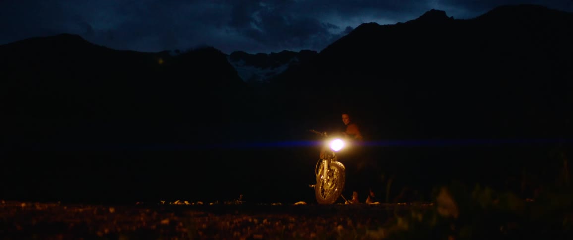 A man is getting on his motorcycle at night