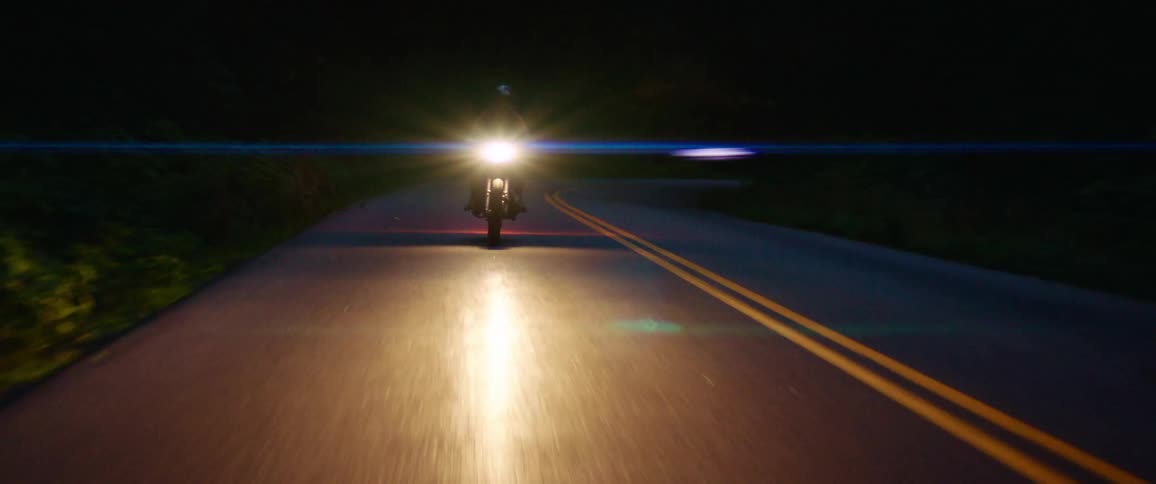 A biker rides a motorcycle along a road through a forest at night